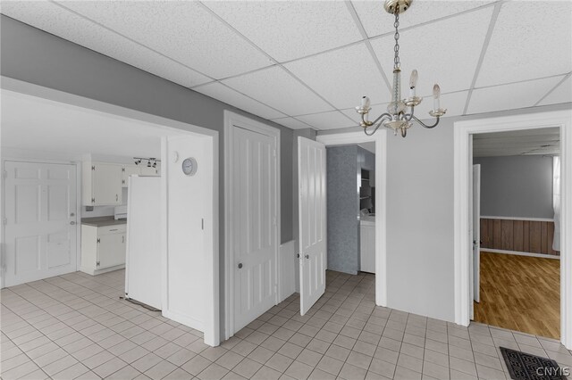 tiled spare room featuring a drop ceiling and an inviting chandelier