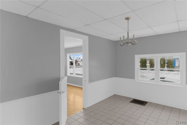 spare room with light tile patterned flooring, an inviting chandelier, and a drop ceiling