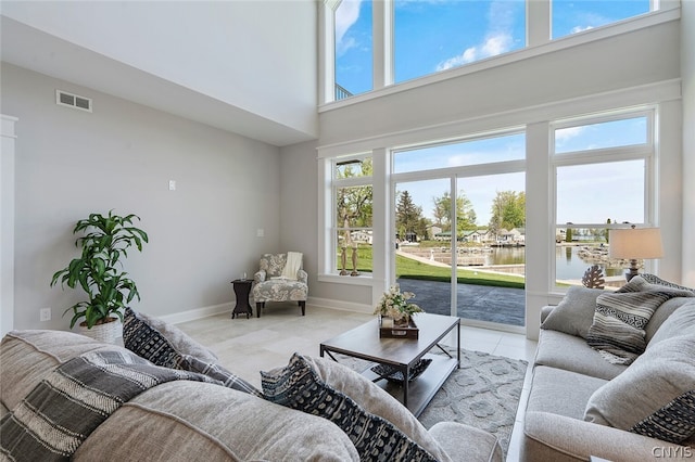 living room with light tile floors, a high ceiling, a healthy amount of sunlight, and a water view