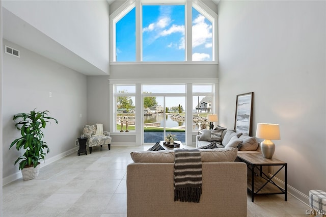 living room with a water view, light tile floors, and a towering ceiling