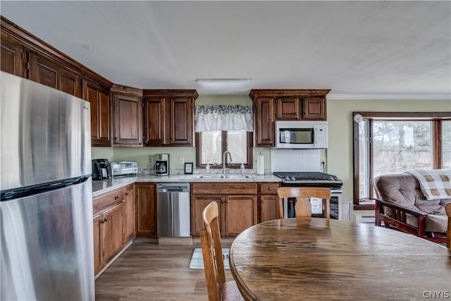 kitchen featuring light stone countertops, appliances with stainless steel finishes, sink, ornamental molding, and light hardwood / wood-style flooring