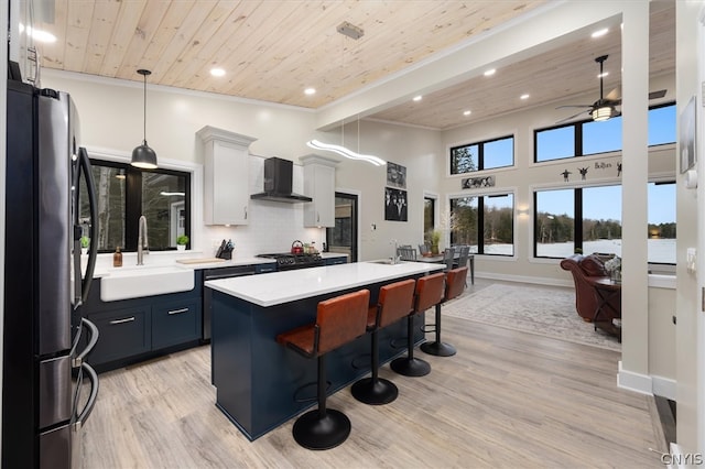 kitchen with stainless steel fridge, a kitchen island with sink, light hardwood / wood-style flooring, wall chimney range hood, and white cabinetry