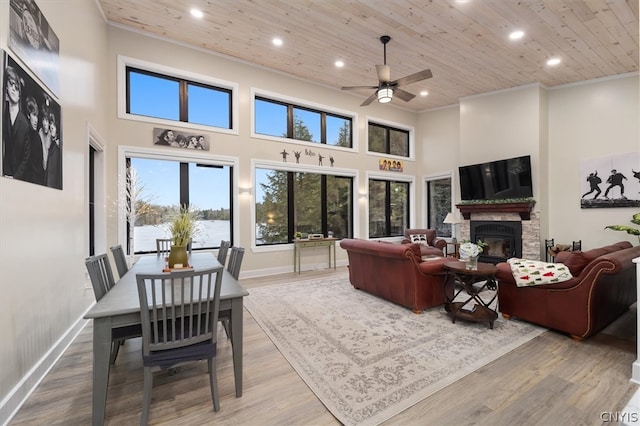 living room with light wood-type flooring, ceiling fan, wooden ceiling, a towering ceiling, and a stone fireplace