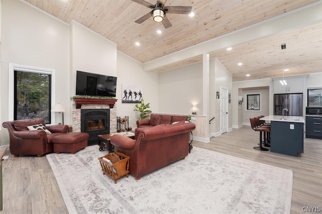 living room with ceiling fan, wooden ceiling, light hardwood / wood-style flooring, a stone fireplace, and high vaulted ceiling