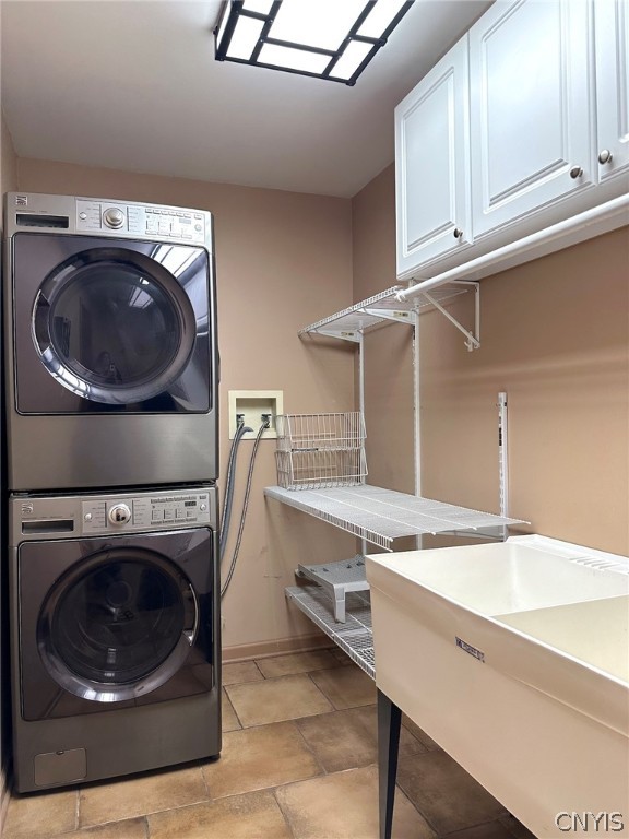 clothes washing area featuring light tile patterned flooring, stacked washer / dryer, and cabinets