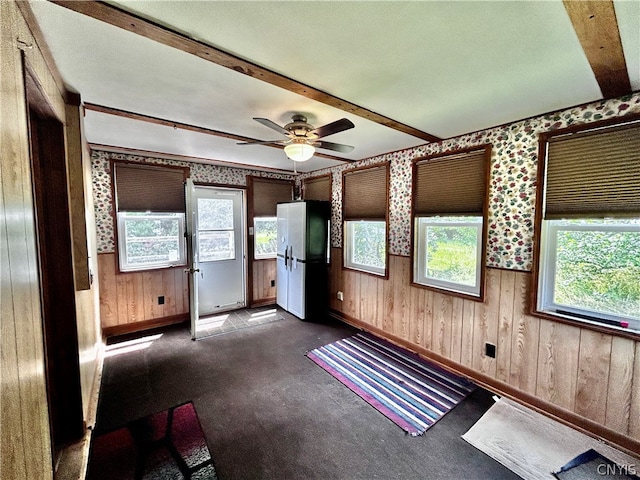 spare room with ceiling fan, wood walls, dark carpet, and beam ceiling