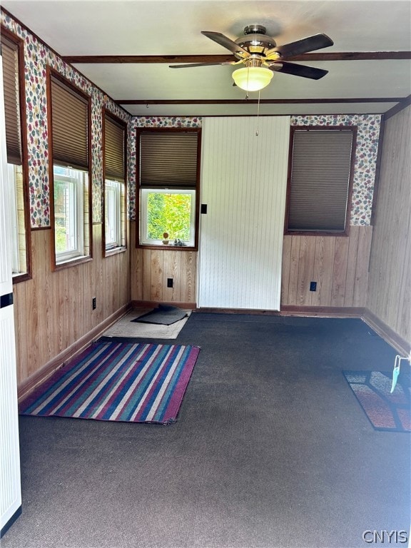 carpeted empty room with plenty of natural light, wooden walls, and ceiling fan