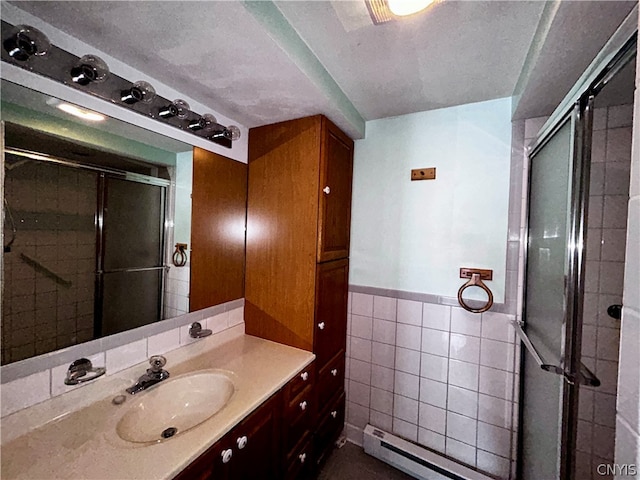 bathroom with tile walls, a shower with door, a textured ceiling, a baseboard heating unit, and vanity