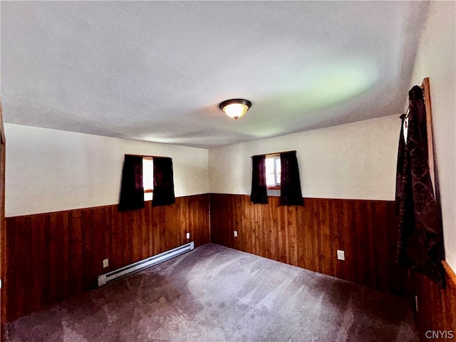 spare room with a textured ceiling, baseboard heating, and dark colored carpet