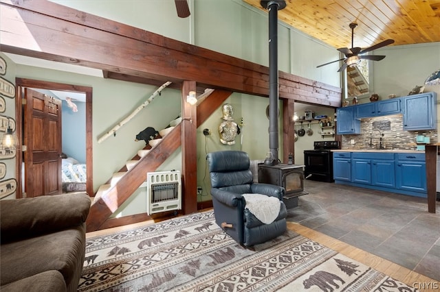 tiled living room featuring a wood stove, ceiling fan, wooden ceiling, high vaulted ceiling, and sink