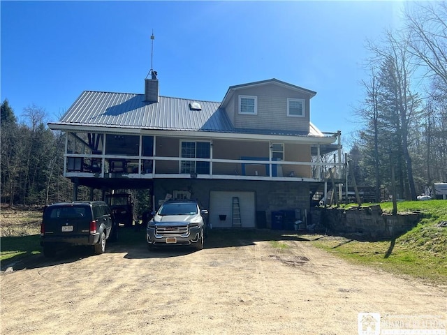 back of property with dirt driveway, metal roof, a chimney, and a garage