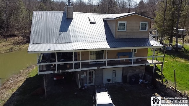 back of property with metal roof, a chimney, and a water view