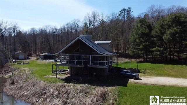 rear view of property featuring metal roof, a sunroom, a yard, a chimney, and a wooded view