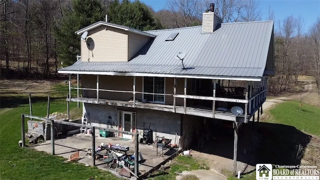 back of house featuring a yard, a chimney, a patio, metal roof, and a balcony