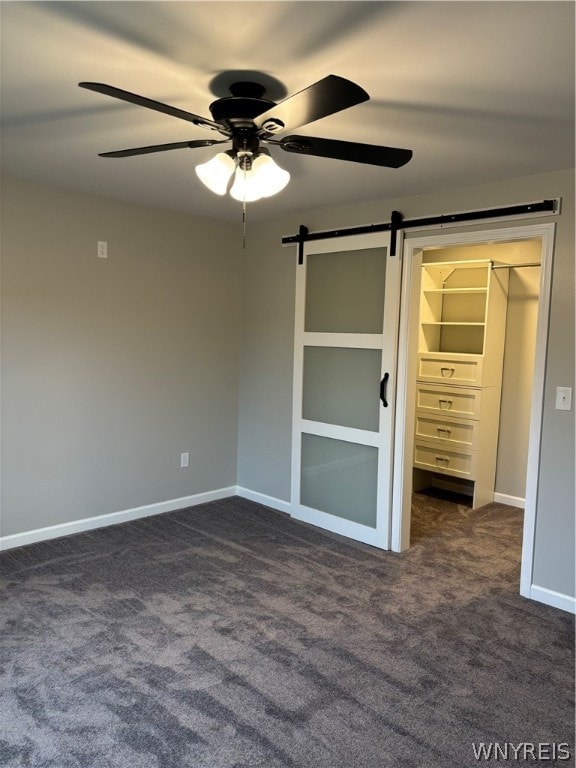 unfurnished bedroom with a closet, dark carpet, ceiling fan, and a walk in closet