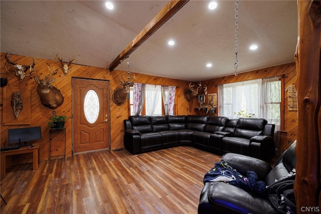 living room featuring wooden walls, a healthy amount of sunlight, beam ceiling, and hardwood / wood-style floors