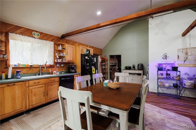 kitchen with wood walls, black appliances, lofted ceiling with beams, sink, and light wood-type flooring