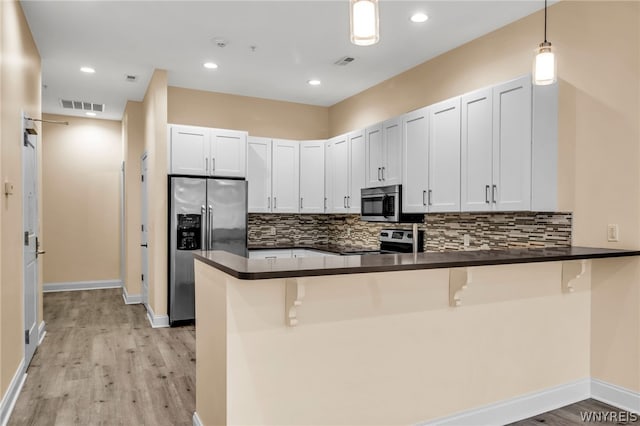 kitchen with backsplash, kitchen peninsula, appliances with stainless steel finishes, and light hardwood / wood-style floors