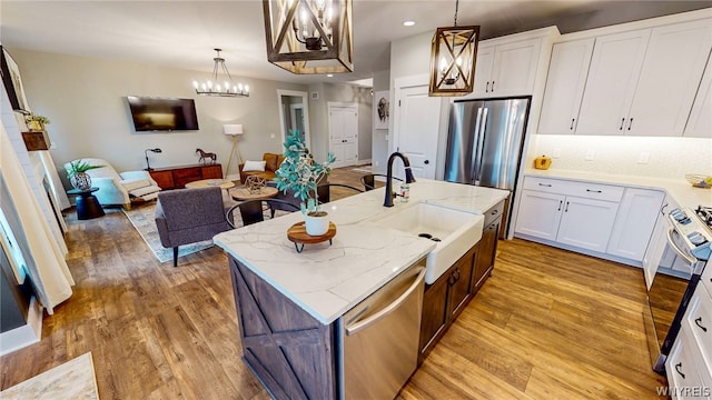 kitchen with stainless steel appliances, a center island with sink, light hardwood / wood-style floors, and white cabinetry