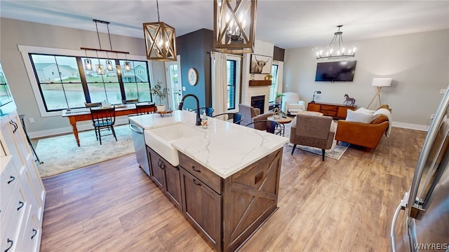 kitchen with a kitchen island with sink, hanging light fixtures, sink, light stone counters, and light hardwood / wood-style floors