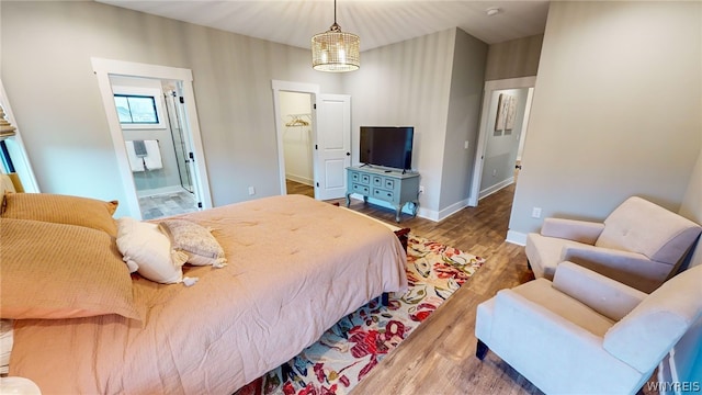 bedroom featuring a walk in closet, hardwood / wood-style flooring, ensuite bathroom, and an inviting chandelier