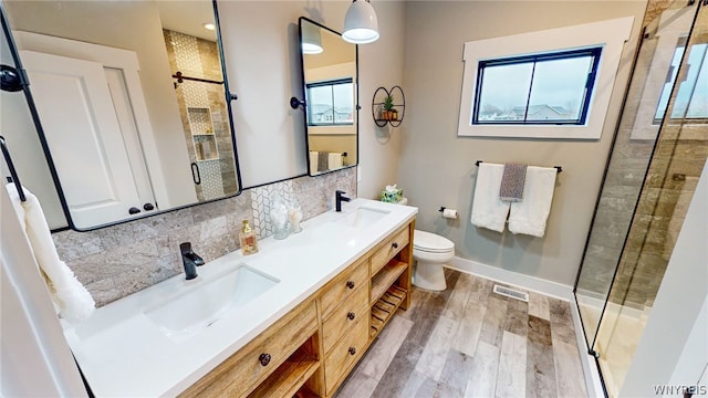 bathroom featuring double sink vanity, backsplash, hardwood / wood-style floors, toilet, and a shower with shower door