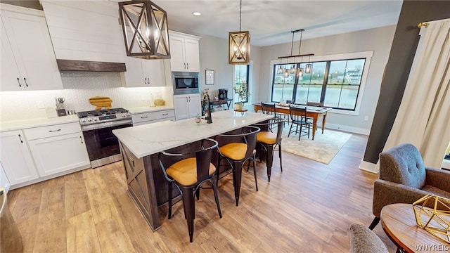 kitchen featuring decorative light fixtures, light wood-type flooring, stainless steel appliances, a kitchen bar, and a center island with sink