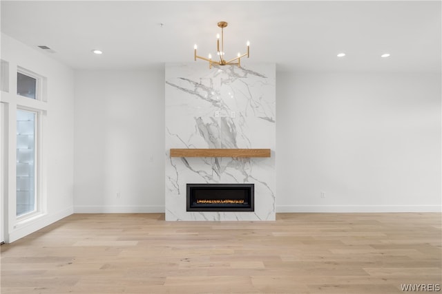 unfurnished living room featuring a chandelier, a premium fireplace, and light wood-type flooring