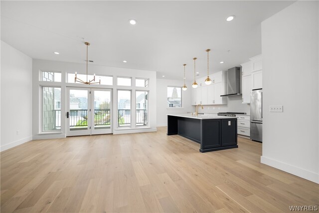 kitchen with plenty of natural light, an island with sink, stainless steel appliances, and wall chimney exhaust hood