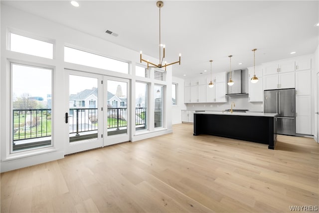 kitchen with a kitchen island with sink, a wealth of natural light, wall chimney range hood, and stainless steel fridge