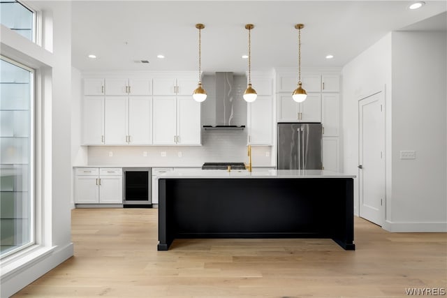 kitchen with wall chimney exhaust hood, wine cooler, stainless steel refrigerator, tasteful backsplash, and light wood-type flooring