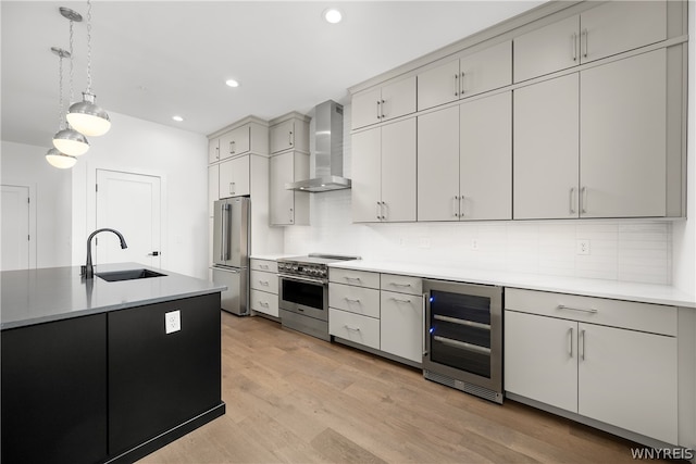 kitchen with appliances with stainless steel finishes, light hardwood / wood-style flooring, beverage cooler, wall chimney exhaust hood, and sink