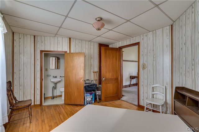 bedroom with ensuite bath, a drop ceiling, light wood-type flooring, and wooden walls