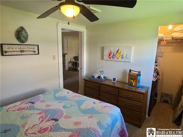 bedroom with a closet, a spacious closet, dark carpet, and ceiling fan