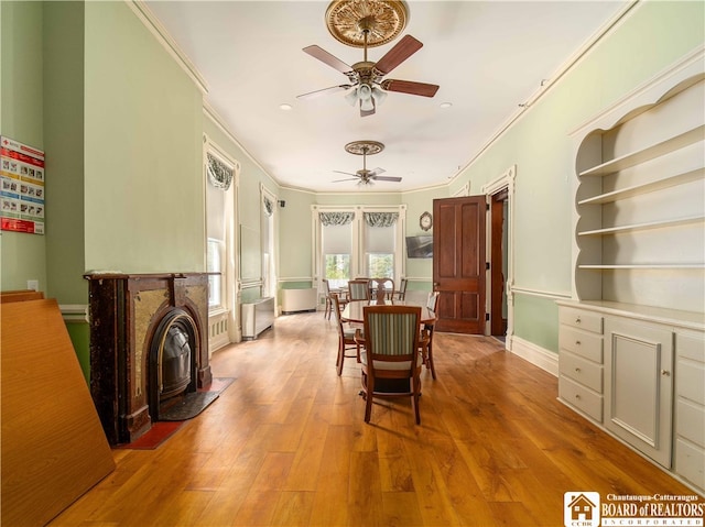 dining area with wood-type flooring, ceiling fan, crown molding, and a wood stove