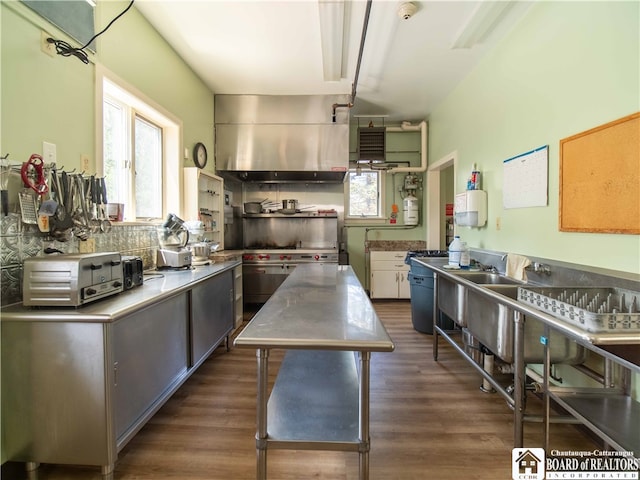 kitchen with stainless steel counters, a center island, dark hardwood / wood-style floors, backsplash, and wall chimney range hood