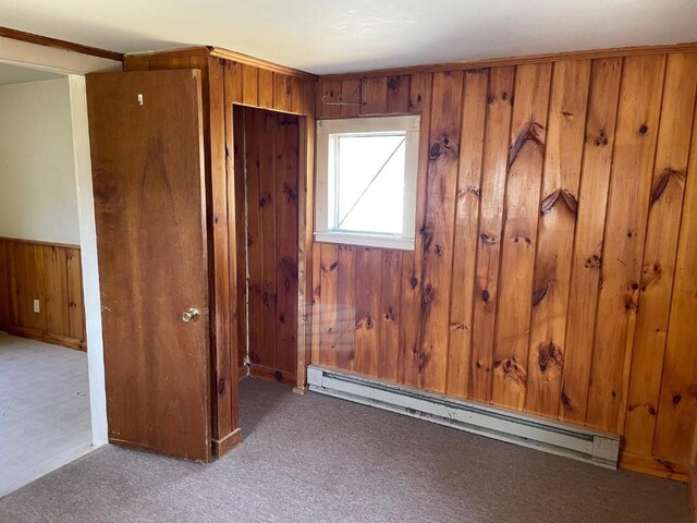 empty room with wooden walls, a baseboard heating unit, and carpet