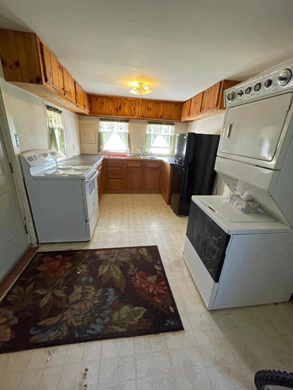 kitchen featuring sink, stacked washer and dryer, light tile flooring, and black refrigerator