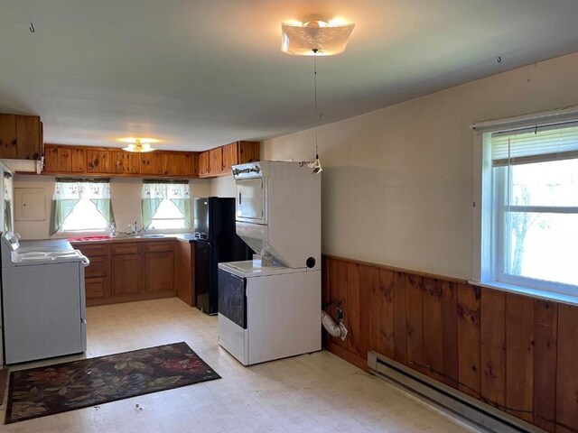 kitchen featuring black refrigerator, a baseboard radiator, light tile floors, white range with electric cooktop, and stacked washer and dryer