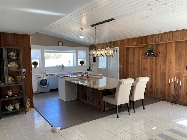 interior space with decorative light fixtures, wood walls, vaulted ceiling, washer / clothes dryer, and light hardwood / wood-style floors