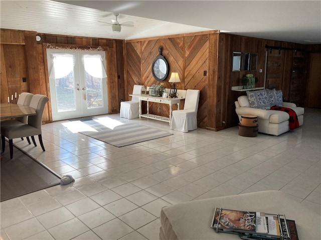 living room with french doors, light tile patterned flooring, wood walls, and ceiling fan