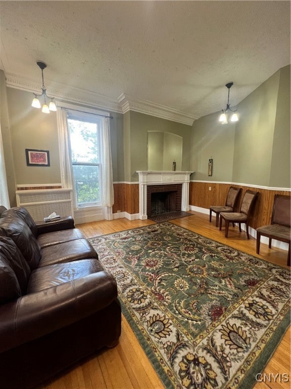 living room with ornamental molding, a brick fireplace, a textured ceiling, a notable chandelier, and hardwood / wood-style floors