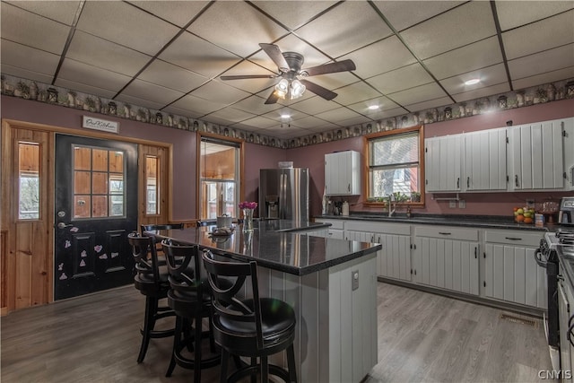 kitchen with light wood-type flooring, stainless steel fridge, a kitchen bar, a kitchen island, and white cabinets