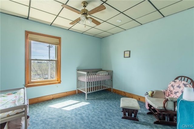 carpeted bedroom with a drop ceiling, ceiling fan, and a crib