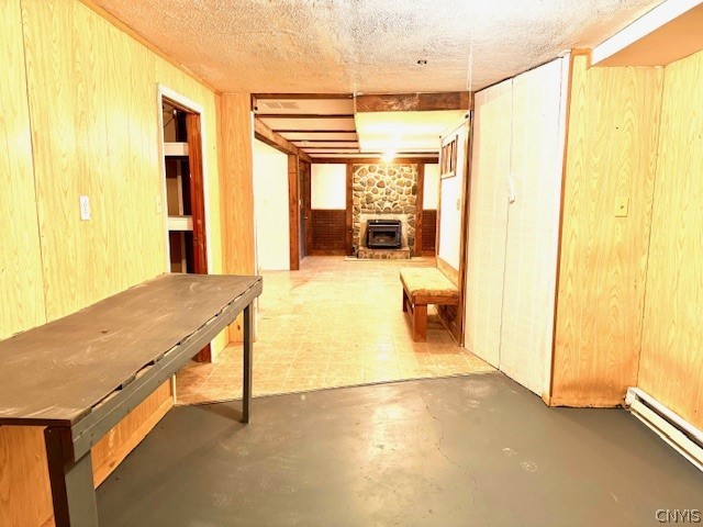 basement featuring a wood stove, a baseboard radiator, wooden walls, and heating unit