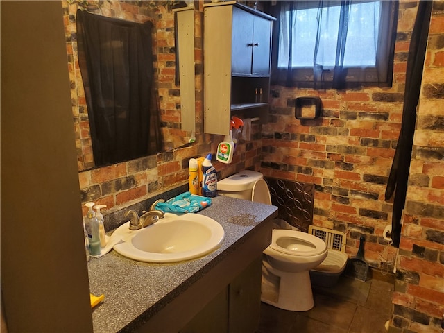 bathroom with brick wall, vanity with extensive cabinet space, toilet, and tile floors