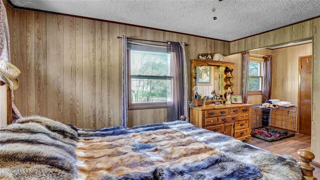 bedroom with wooden walls, multiple windows, a textured ceiling, and hardwood / wood-style flooring