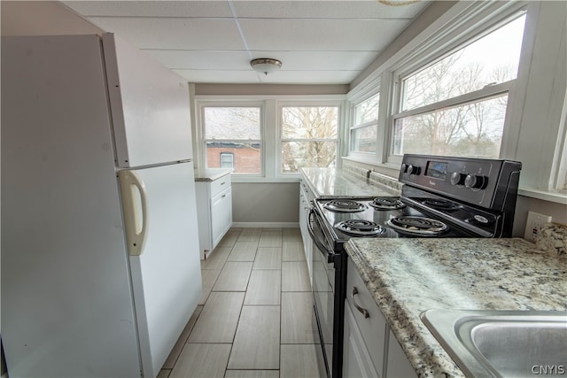 kitchen featuring black range with electric cooktop, white cabinetry, white fridge, light tile floors, and light stone counters