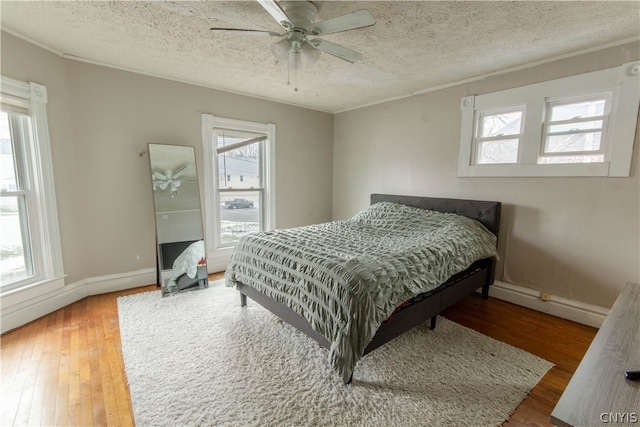 bedroom with a textured ceiling, hardwood / wood-style floors, ceiling fan, and multiple windows