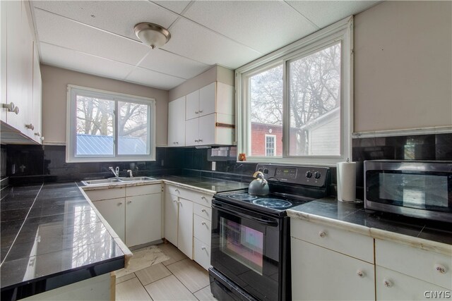 kitchen with light tile flooring, white cabinetry, a drop ceiling, black electric range, and tasteful backsplash